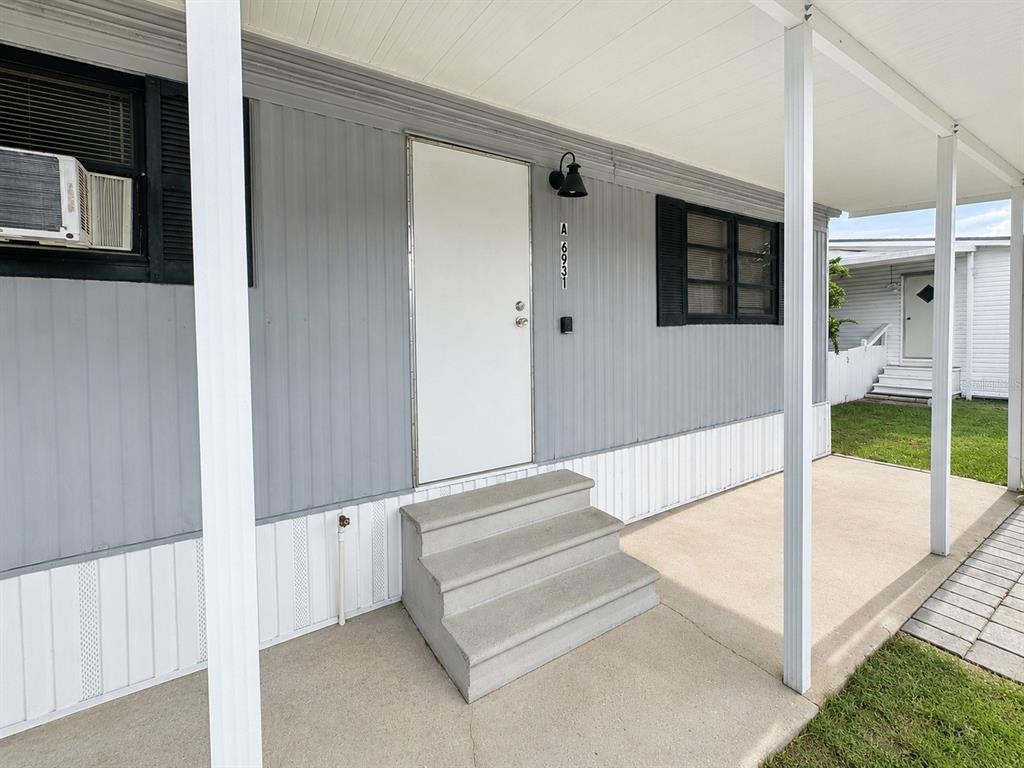 A gray mobile home exterior features a white door, concrete steps, and a covered porch — 6931 POMPEII ROAD, ORLANDO, FL