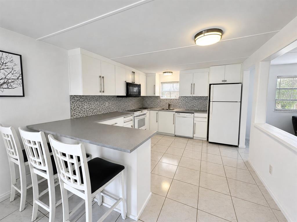 A kitchen with white cabinets, gray countertops, a tiled backsplash, and a breakfast bar — 6931 POMPEII ROAD, ORLANDO, FL