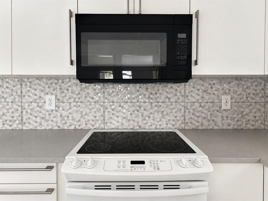 A white electric stove sits below a black over-the-range microwave against a hexagonal tile backsplash — 6931 POMPEII ROAD, ORLANDO, FL