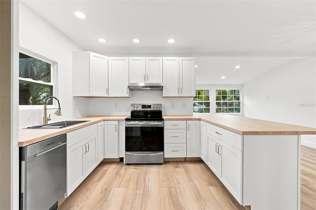 A kitchen features white cabinets, light wood countertops, stainless steel appliances, and wood-look flooring — 1468 19TH STREET, SARASOTA, FL