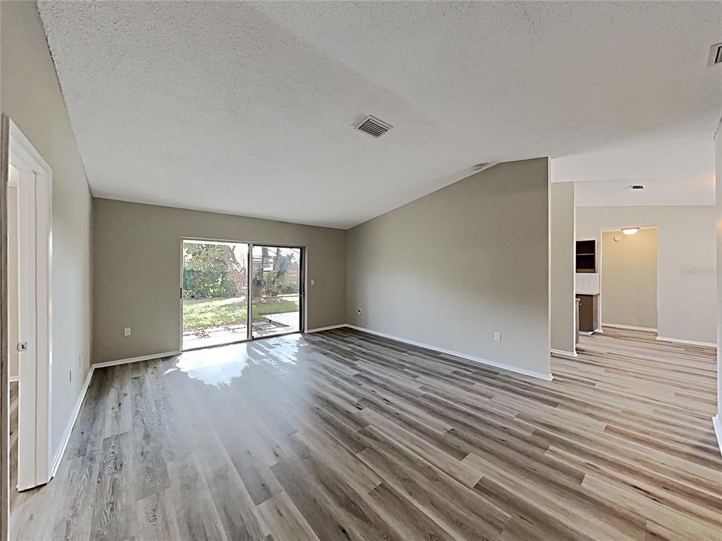 A living room with light gray walls, wood-look flooring, and a sliding glass door — 3205 40TH STREET W, BRADENTON, FL