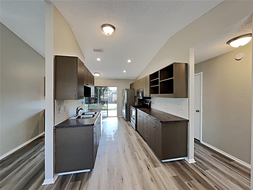 A galley kitchen features dark brown cabinets, dark countertops, and light wood-look flooring — 3205 40TH STREET W, BRADENTON, FL