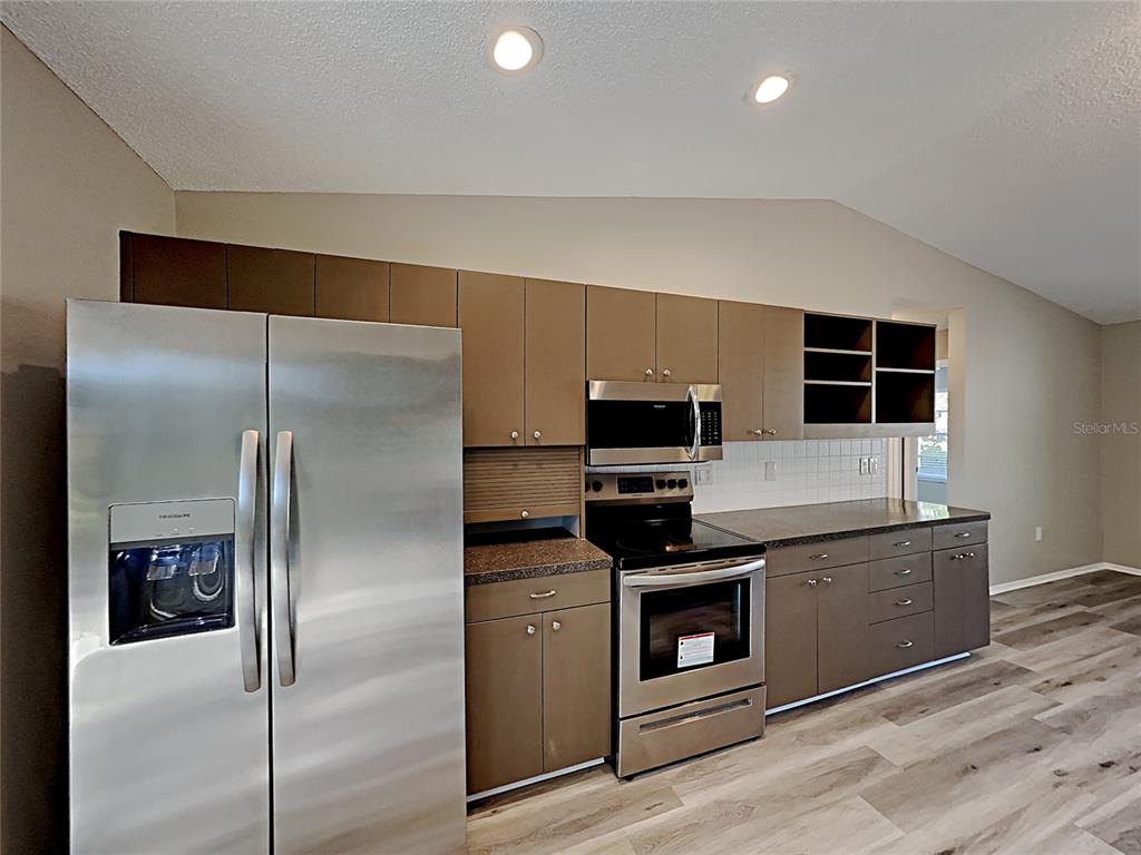 A kitchen features stainless steel appliances, brown cabinets, dark countertops, and light wood-look flooring — 3205 40TH STREET W, BRADENTON, FL