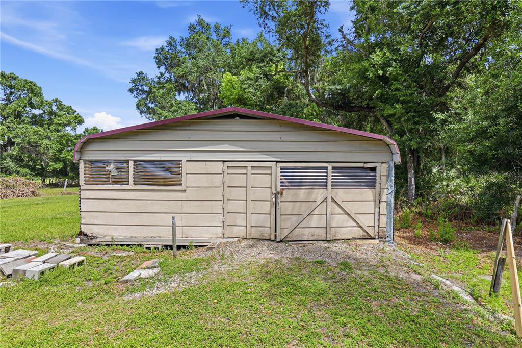 A beige metal shed with a red roof sits on a grassy lot near trees — 403 WENDEL AVENUE, LITHIA, FL