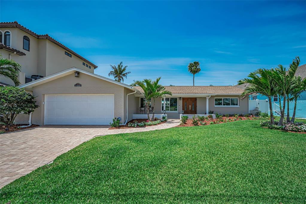 A single-story house with a white garage, brick driveway, and palm trees in the front yard — 11800 7TH STREET E, TREASURE ISLAND, FL