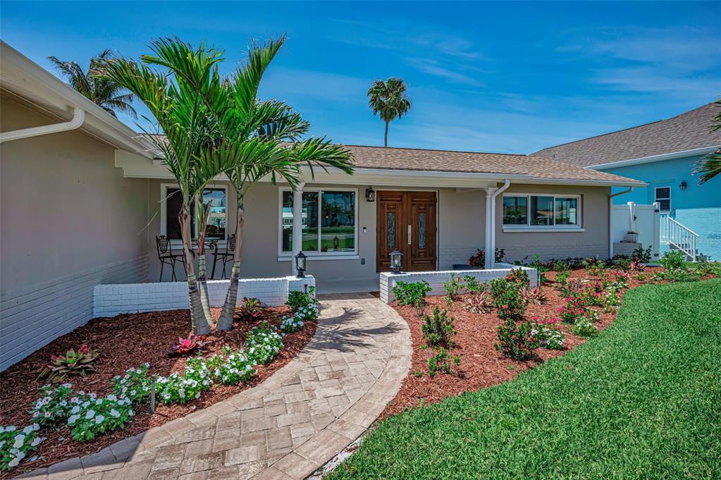 A paved walkway leads to the front entrance of a single-story house with landscaping — 11800 7TH STREET E, TREASURE ISLAND, FL