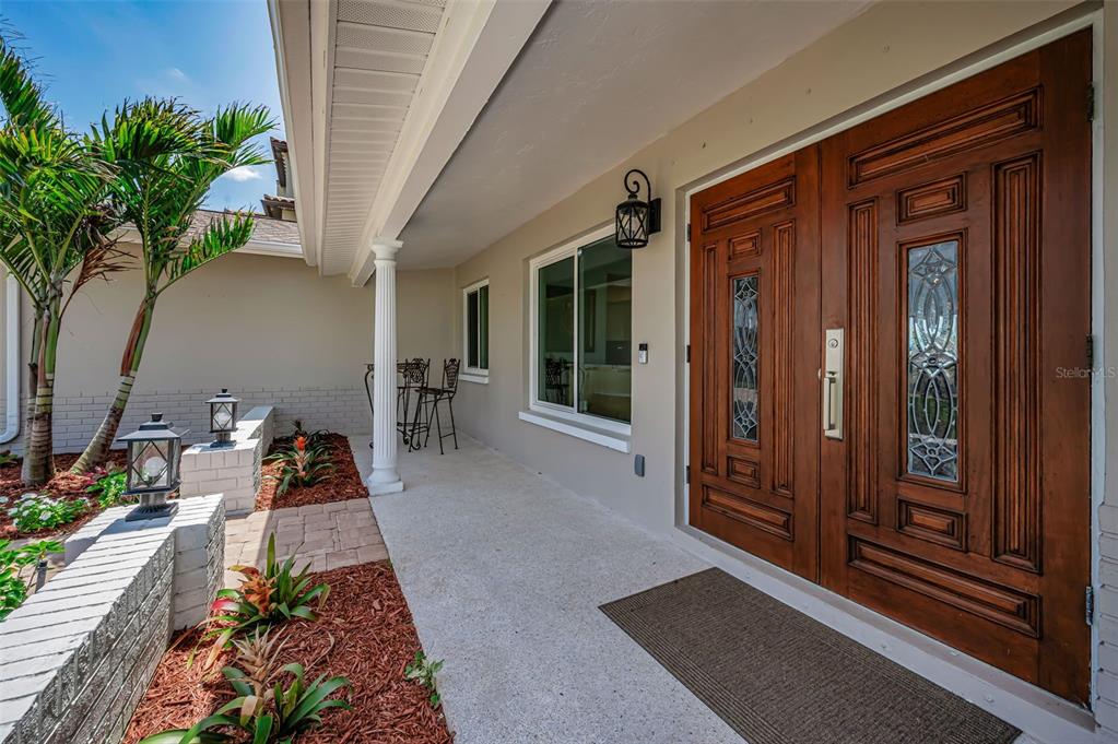 A covered front porch features a double wooden door with glass panels and landscaping — 11800 7TH STREET E, TREASURE ISLAND, FL