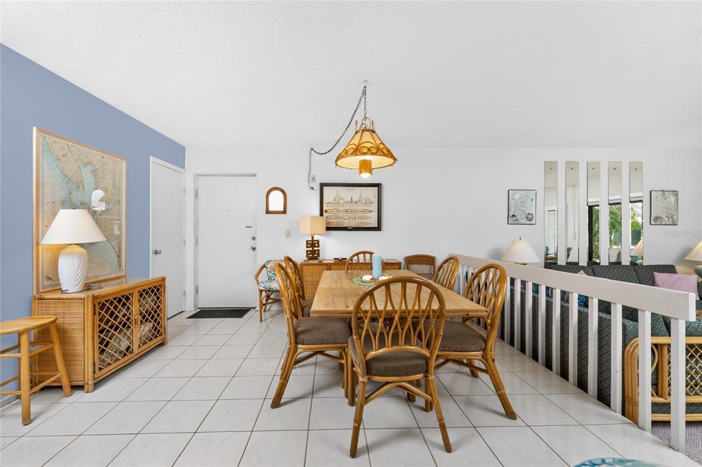 A dining area with a wooden table, rattan chairs, tile flooring, and a hanging pendant light — 2955 N BEACH ROAD UNIT B-614, ENGLEWOOD, FL