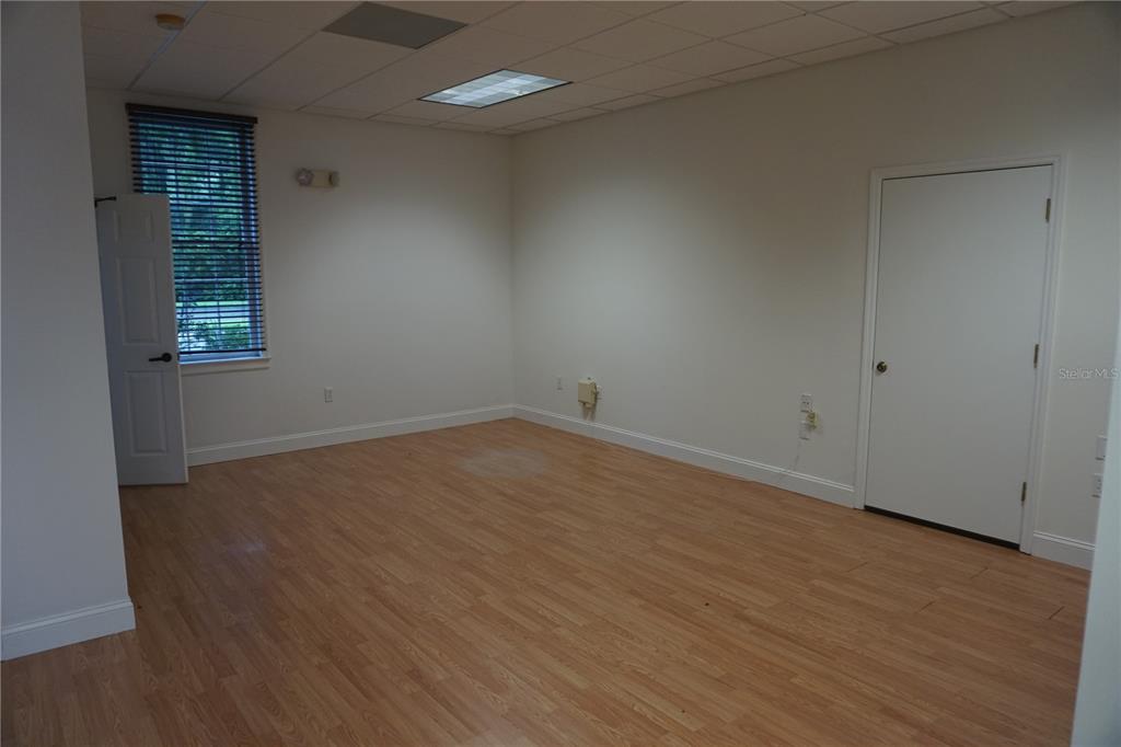 An empty office with light wood-look flooring, white walls, a window with blinds, and doors — 9111 SW 91ST TERRACE, GAINESVILLE, FL