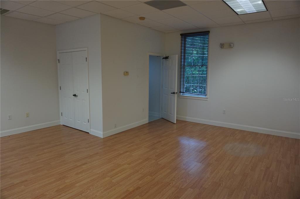 An empty office space features light wood-look flooring, white walls, a window, and two doors — 9111 SW 91ST TERRACE, GAINESVILLE, FL