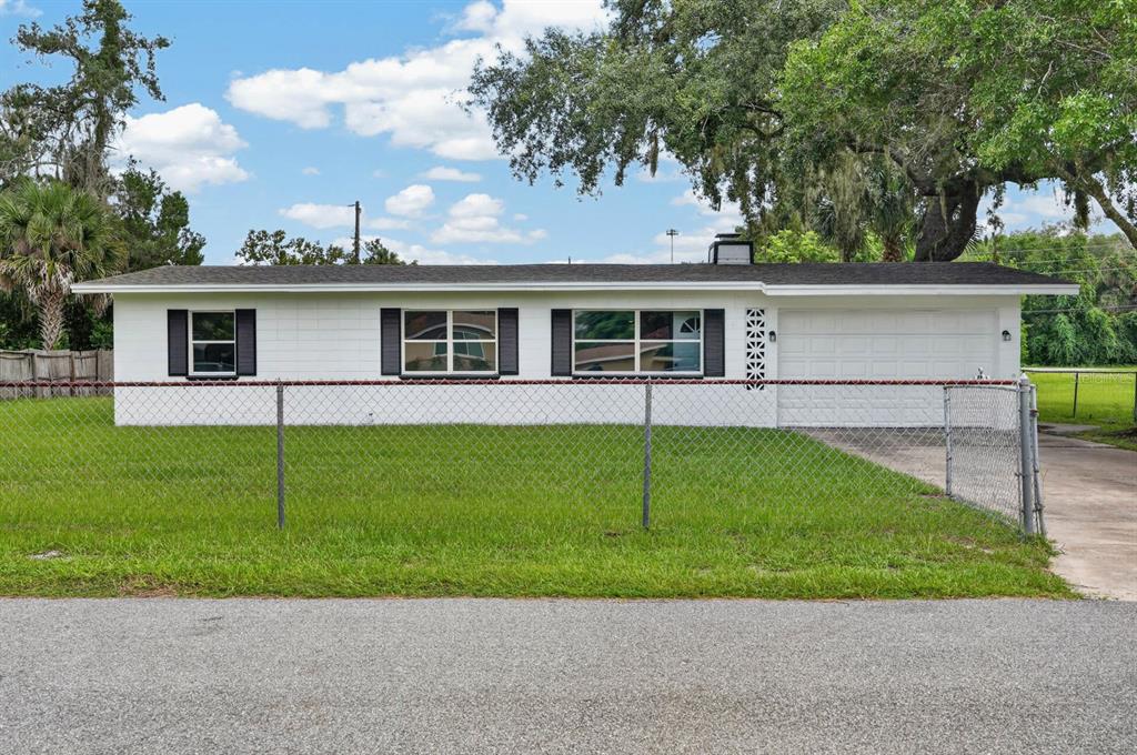 A single-story white house with a black roof, attached garage, and chain-link fence — 7 JEANETTE DRIVE, DELAND, FL