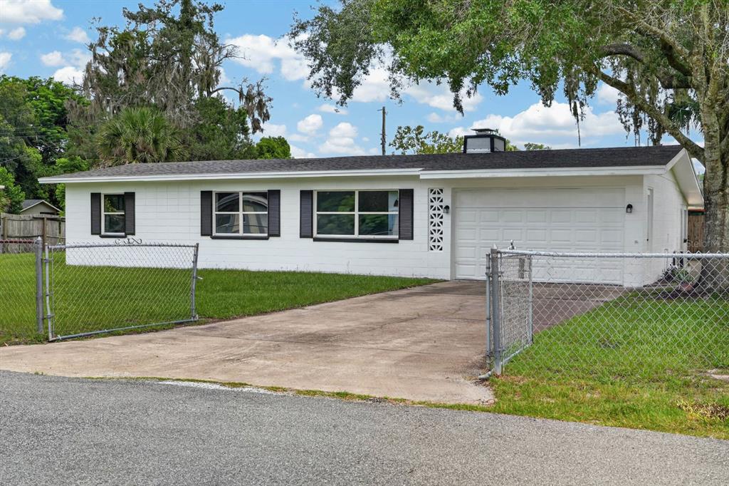 A white, single-story house with a concrete driveway and a chain-link fence in the front — 7 JEANETTE DRIVE, DELAND, FL