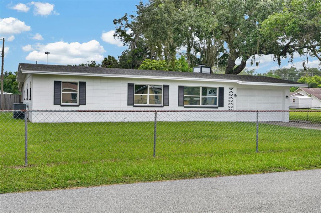 A white, single-story house with a chain-link fence and a large oak tree in front — 7 JEANETTE DRIVE, DELAND, FL