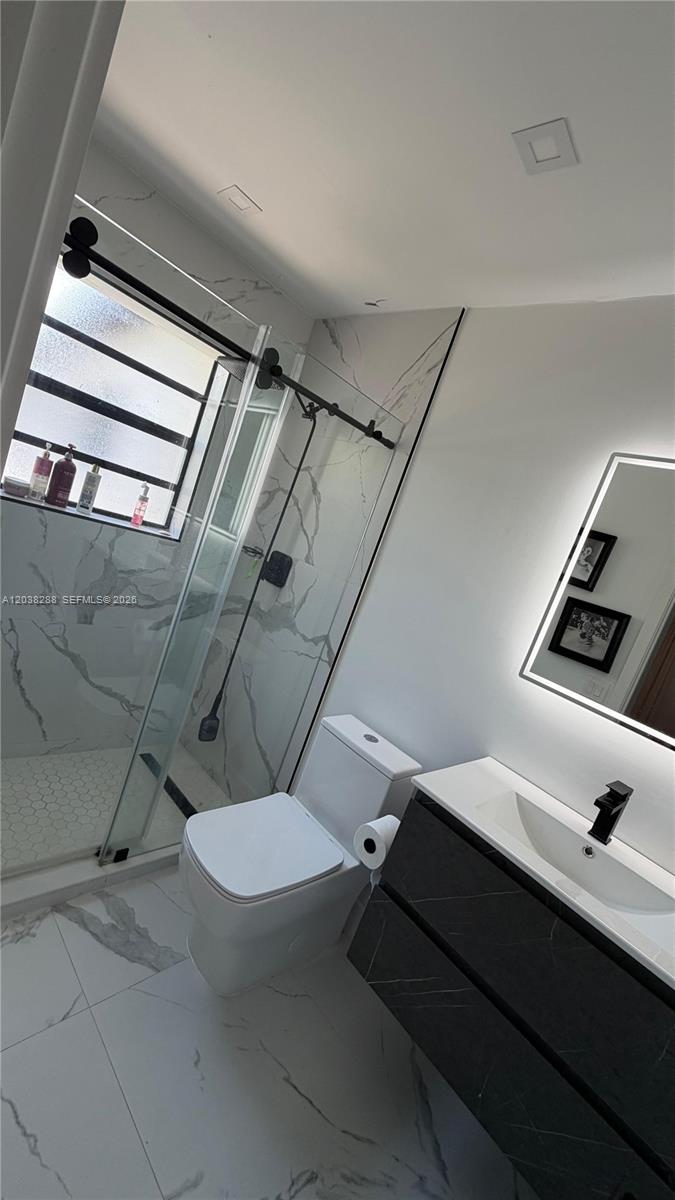 A modern bathroom features a glass-enclosed shower, a white toilet, and a dark vanity — 4161 NE 17th Ave, Pompano Beach FL 33064, POMPANO BEACH, FL