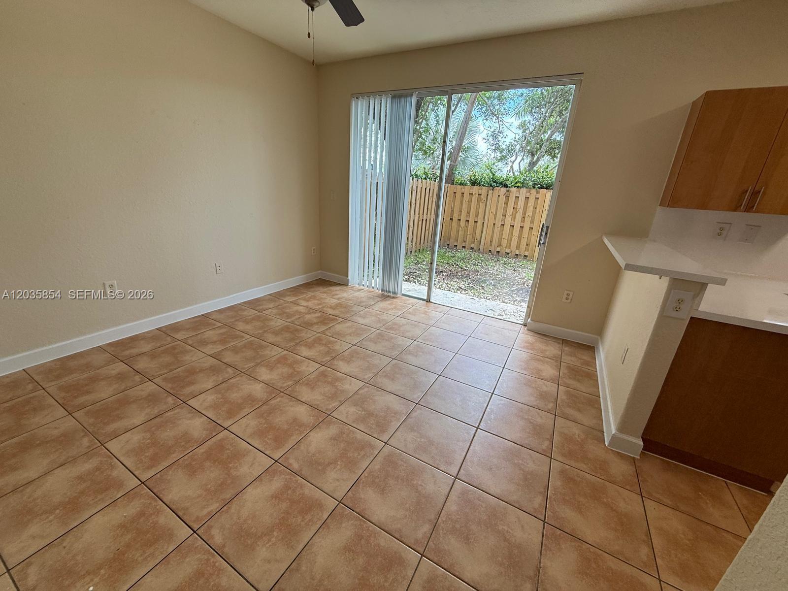 An empty room features tan tile flooring, a sliding glass door, and a kitchen counter — 2462 SE 15th Ct, Homestead FL 33035, HOMESTEAD, FL