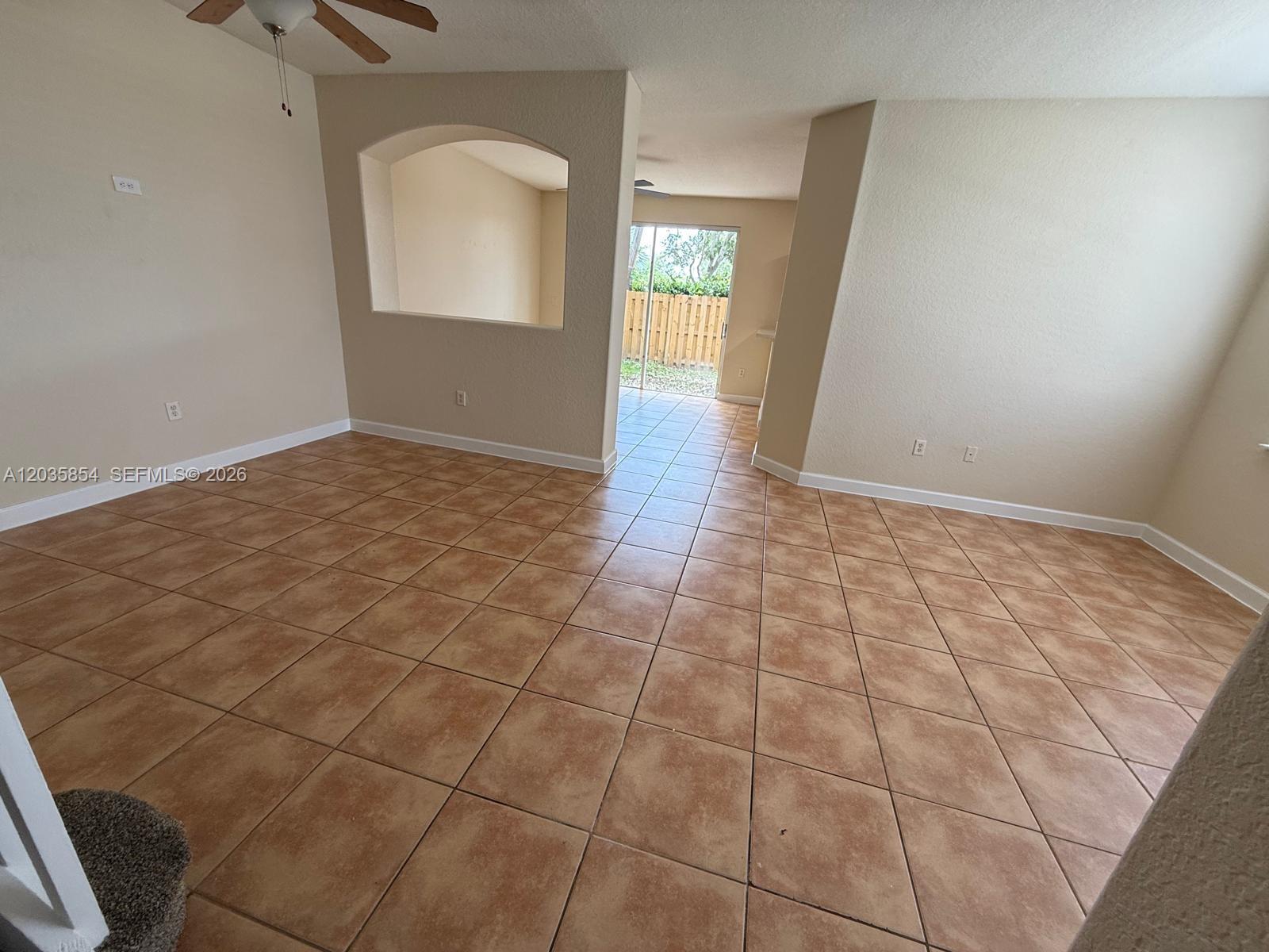 An empty room with tan tile flooring, an arched wall cutout, and a sliding glass door — 2462 SE 15th Ct, Homestead FL 33035, HOMESTEAD, FL