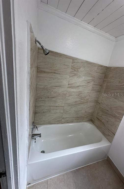 A white bathtub with a shower head is surrounded by beige, wood-look tiled walls — 1238 HERSCHELL STREET, LAKELAND, FL