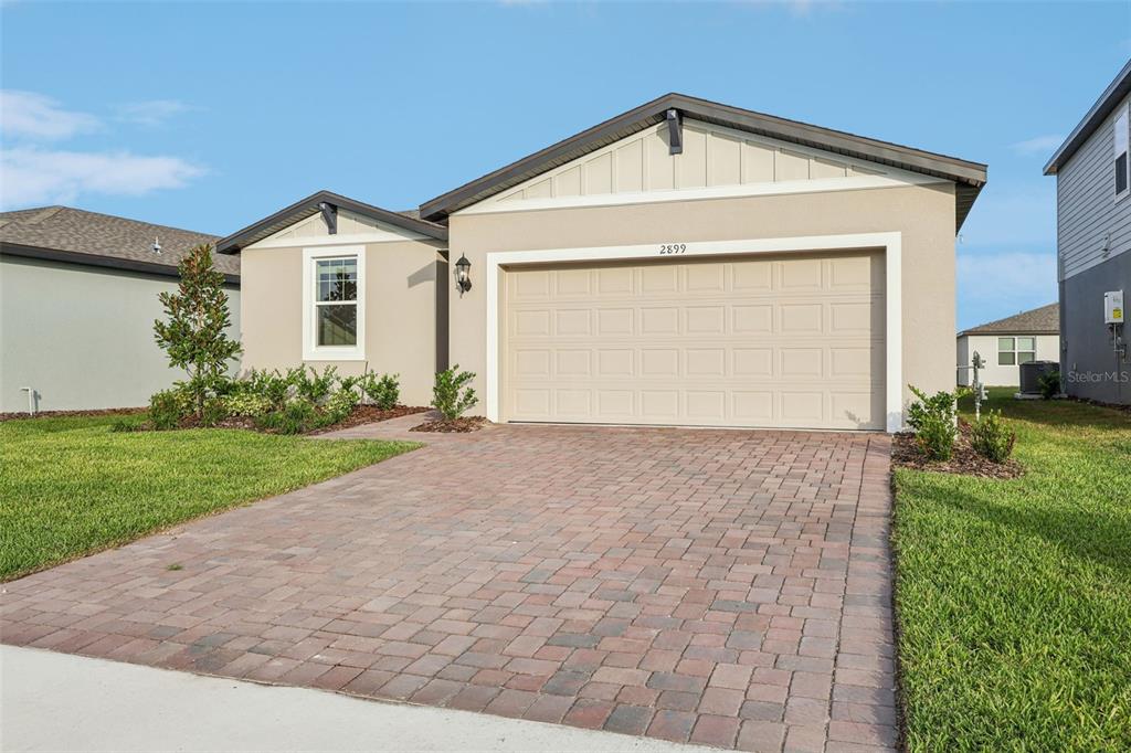 A single-story house with a beige stucco exterior, a two-car garage, and a paver driveway — 2899 HORNBILL DRIVE, ST CLOUD, FL
