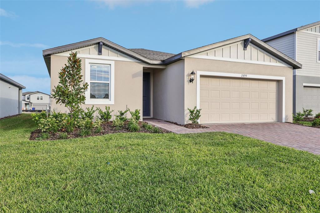 A single-story house with a beige stucco exterior, a two-car garage, and a paved walkway — 2899 HORNBILL DRIVE, ST CLOUD, FL