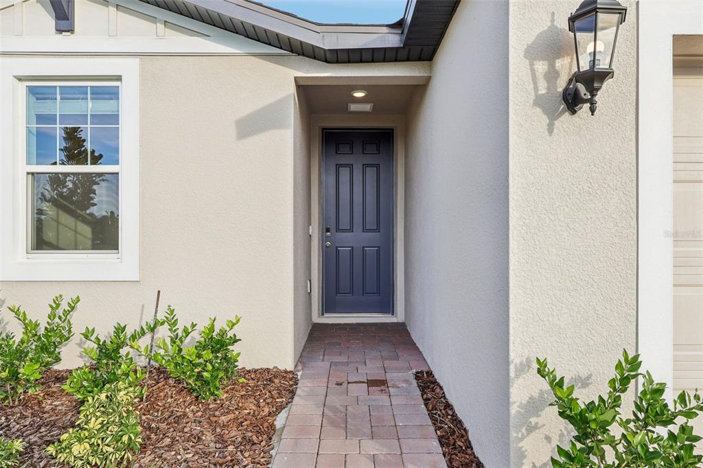 A dark blue front door is recessed into a beige stucco home with a brick walkway — 2899 HORNBILL DRIVE, ST CLOUD, FL