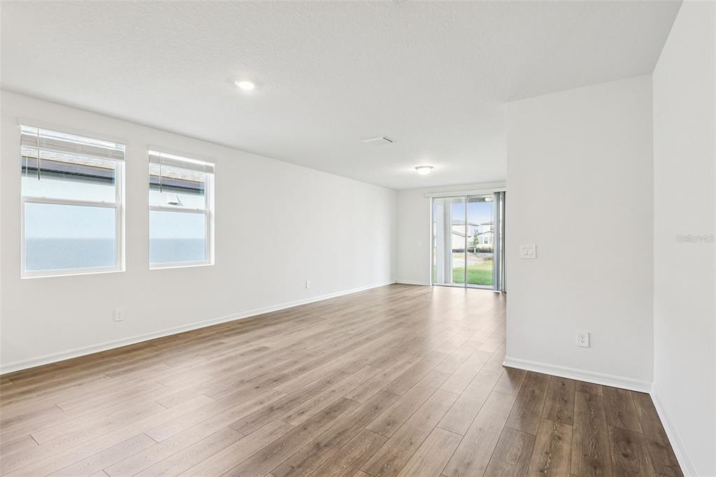An empty room with white walls, wood-look flooring, two windows, and a sliding glass door — 2899 HORNBILL DRIVE, ST CLOUD, FL