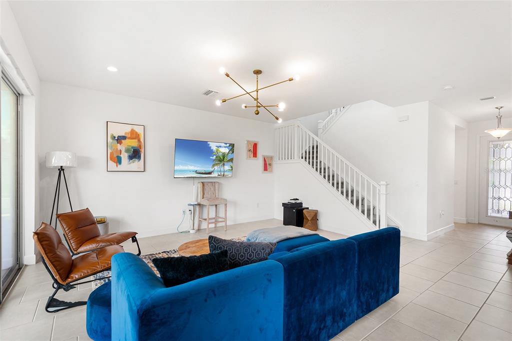 A living room features a blue sectional, two leather chairs, a wall-mounted television, and stairs — 3101 HOLLOW HICKORY PLACE, WESLEY CHAPEL, FL