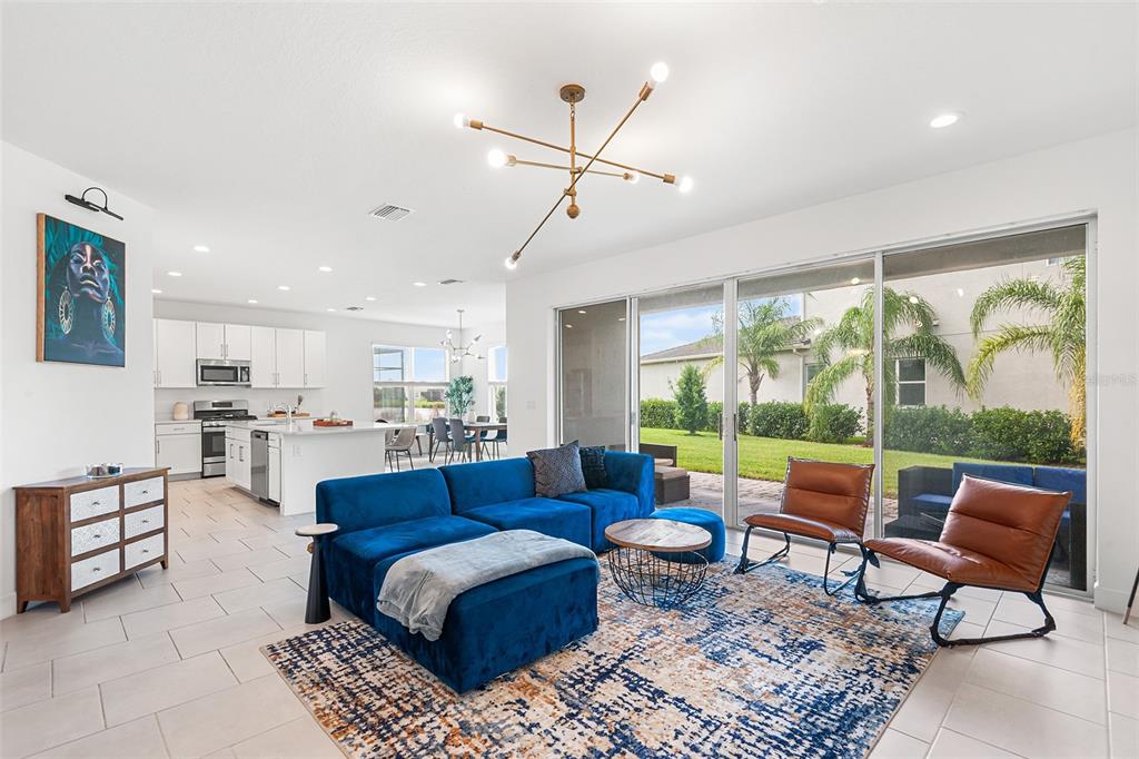 A bright, open-concept living room features a blue sectional, leather chairs, and a sliding glass door — 3101 HOLLOW HICKORY PLACE, WESLEY CHAPEL, FL