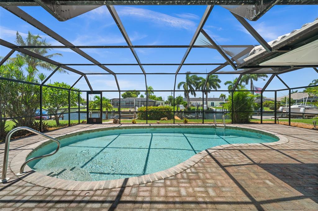 A screened-in pool area with brick pavers overlooks a canal with boat docks and palm trees — 4102 SE 1ST PLACE, CAPE CORAL, FL