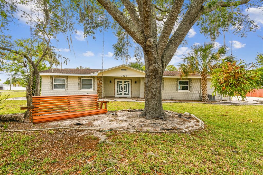 A single-story brick house with a large tree and a wooden swing in the yard — 1302 BRANDONWOOD DRIVE, BRANDON, FL