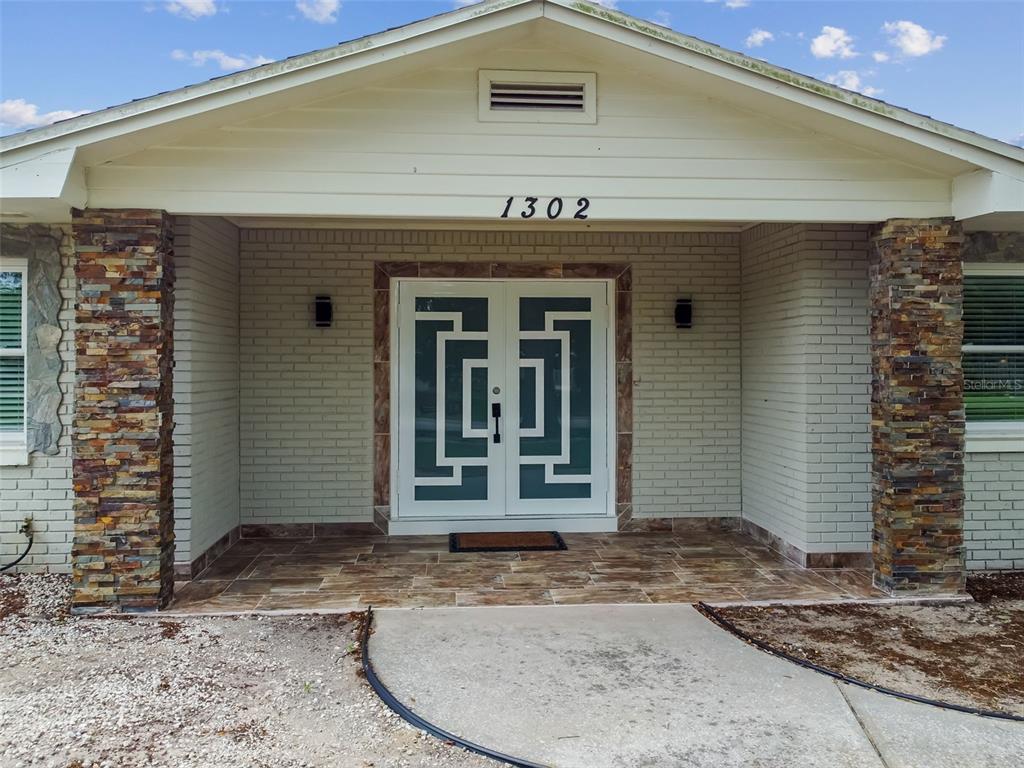 The front exterior of a house features a stone-accented porch and double glass entry doors — 1302 BRANDONWOOD DRIVE, BRANDON, FL