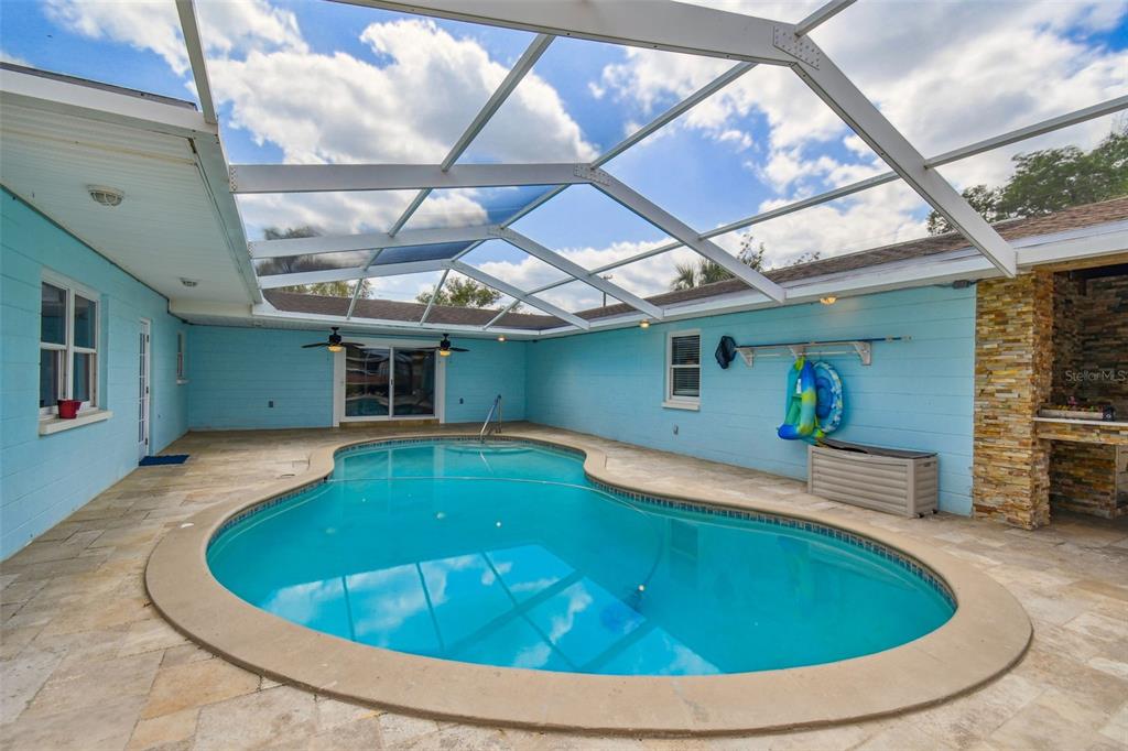 A screened-in patio features a kidney-shaped swimming pool surrounded by light-colored stone pavers — 1302 BRANDONWOOD DRIVE, BRANDON, FL