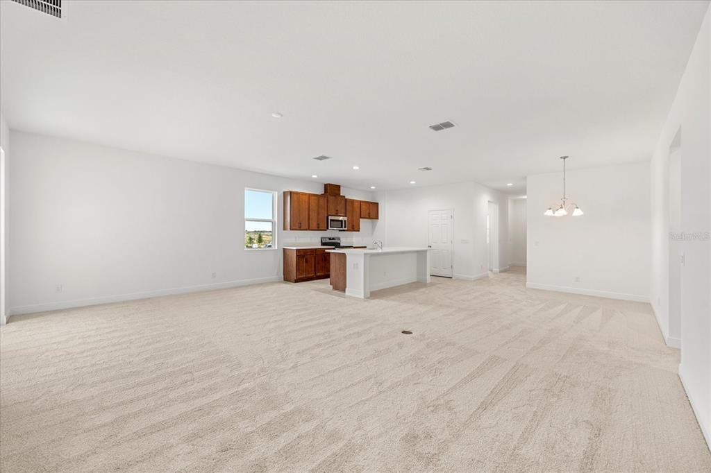 An open-concept living area features beige carpeting, a kitchen with wood cabinets, and an island — 7991 SYRACUSE DRIVE, CLERMONT, FL