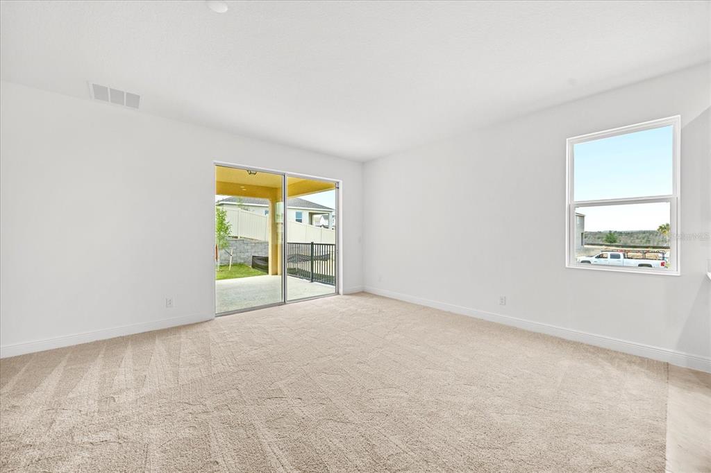 An empty room with beige carpet, white walls, a sliding glass door, and one window — 7991 SYRACUSE DRIVE, CLERMONT, FL
