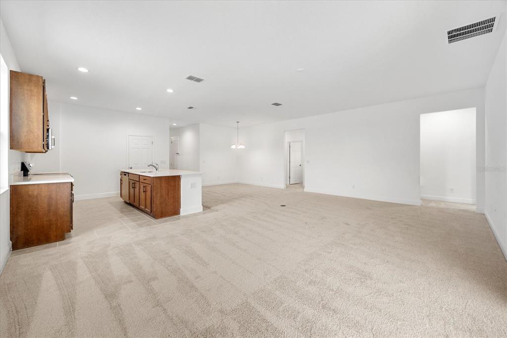 A kitchen with wooden cabinets and an island opens into a large carpeted living area — 7991 SYRACUSE DRIVE, CLERMONT, FL