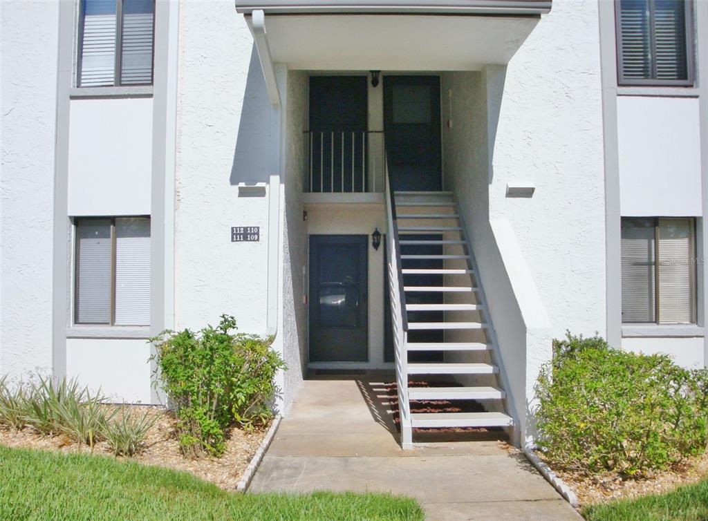 A white stucco apartment building exterior features a ground-level entrance and an outdoor staircase — 111 E CYPRESS COURT UNIT 111, OLDSMAR, FL