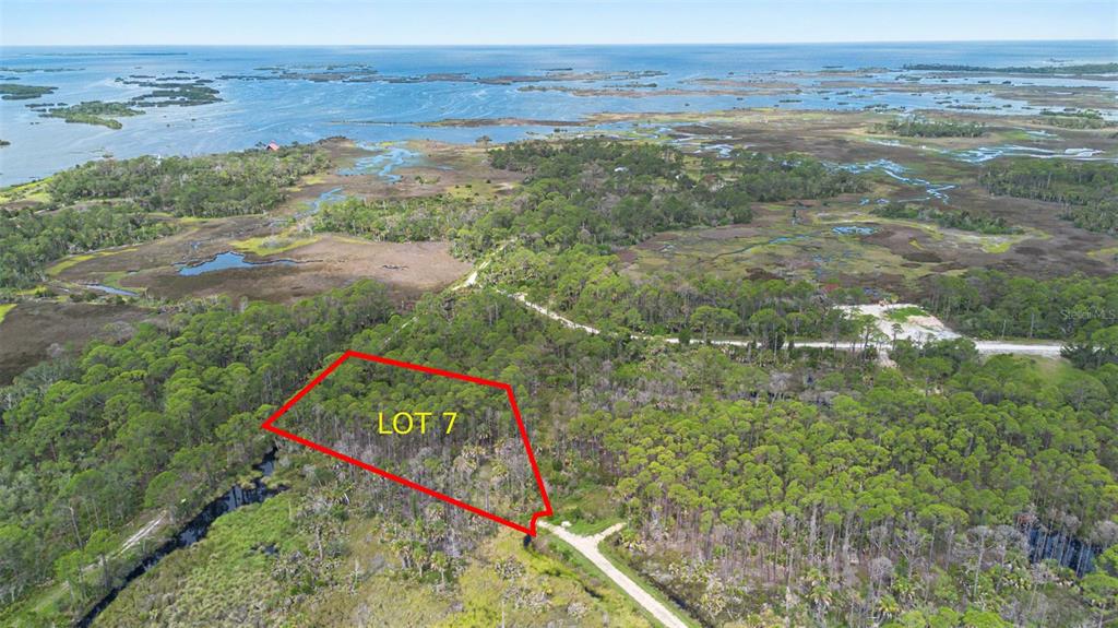 An aerial view shows a wooded lot outlined in red near a coastal marsh — Lot 7 SW 104 STREET, CEDAR KEY, FL