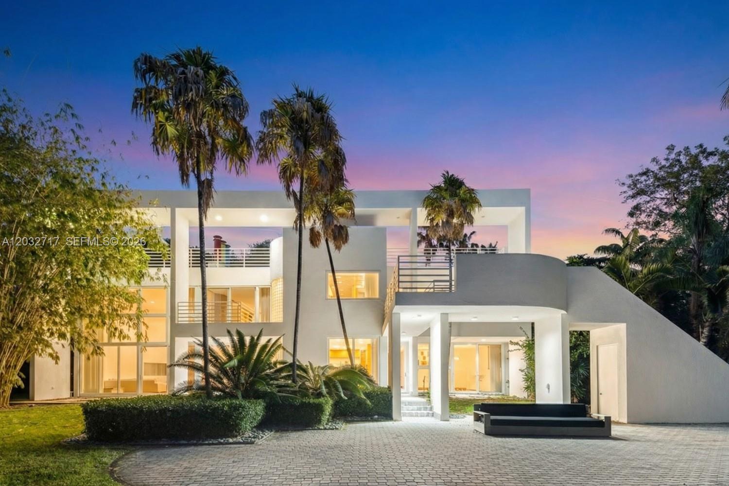 A modern white multi-story house with a curved balcony and palm trees at dusk — 6070 SW 128th St, Pinecrest FL 33156, PINECREST, FL