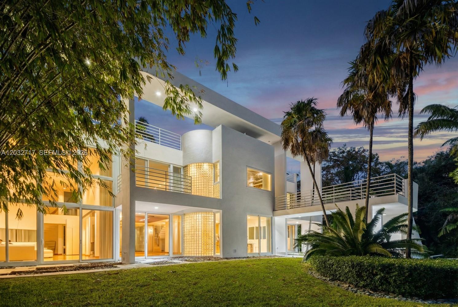A modern white two-story house with glass block walls, balconies, and palm trees at dusk — 6070 SW 128th St, Pinecrest FL 33156, PINECREST, FL