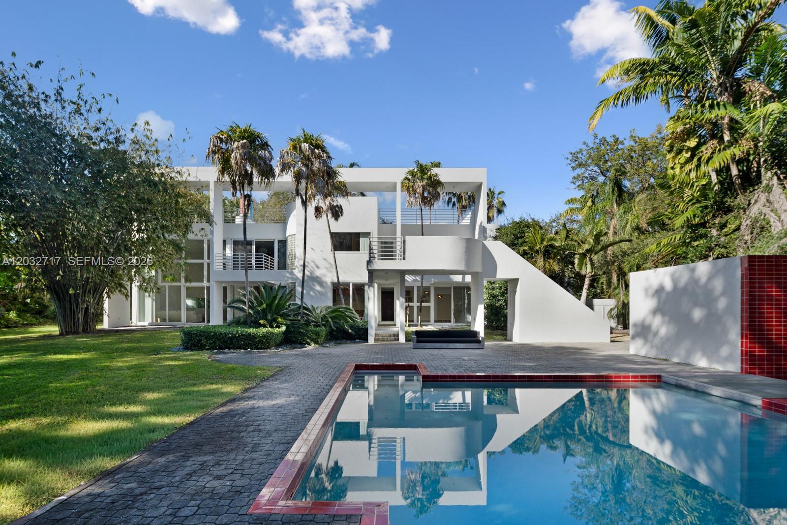 A modern white multi-story house features a swimming pool and a paved patio area — 6070 SW 128th St, Pinecrest FL 33156, PINECREST, FL