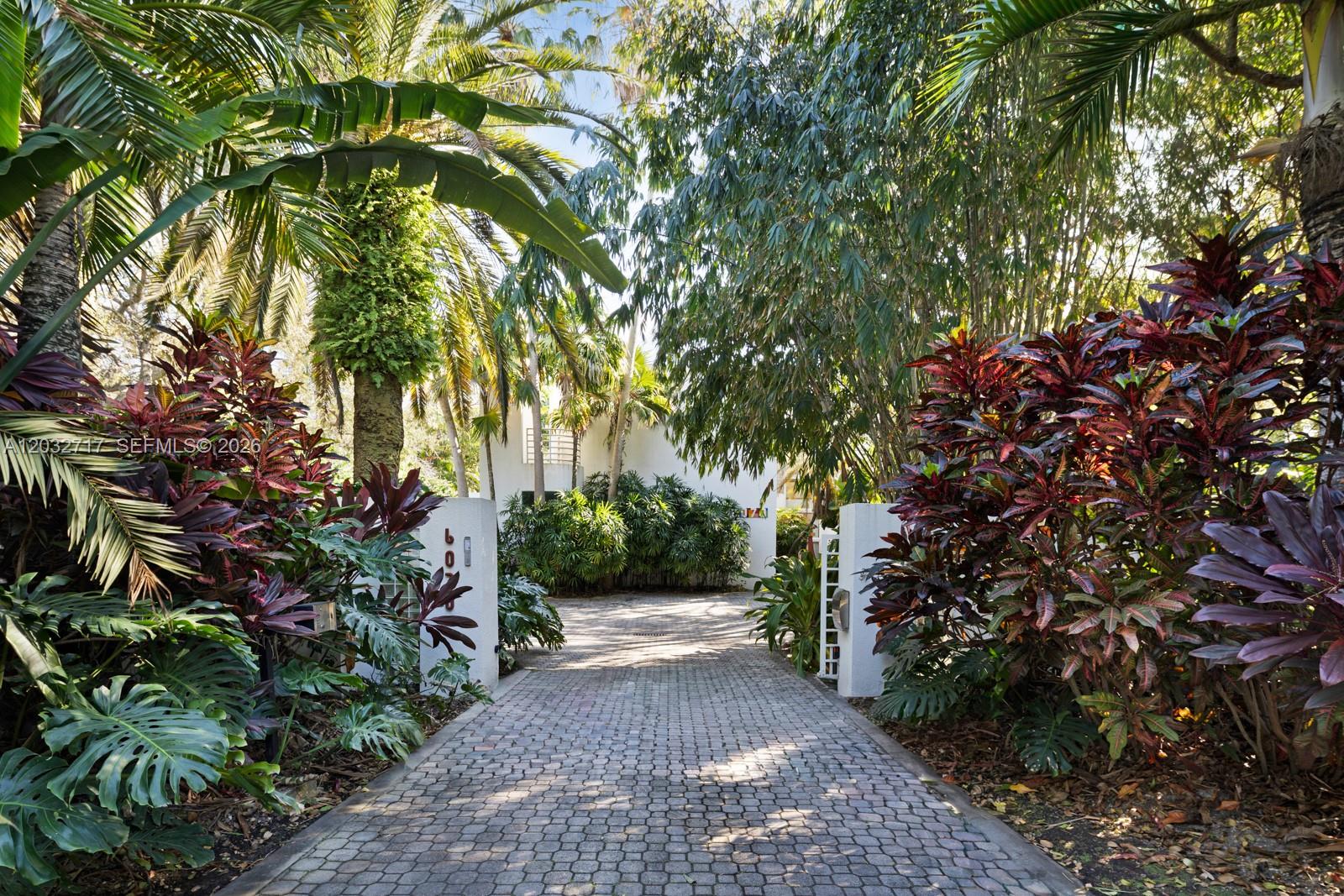 A paved driveway leads toward a white building entrance framed by lush tropical landscaping — 6070 SW 128th St, Pinecrest FL 33156, PINECREST, FL