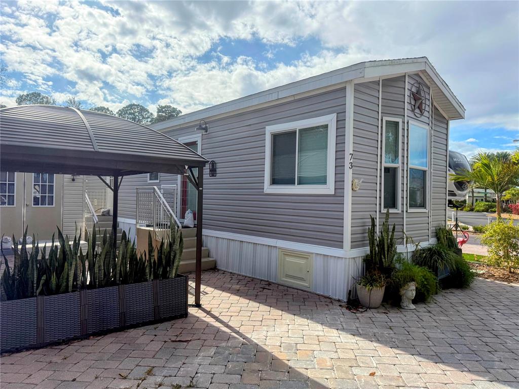 A gray mobile home with a metal gazebo and a paved patio area — 16540 SUNSHINE AVENUE, CLERMONT, FL