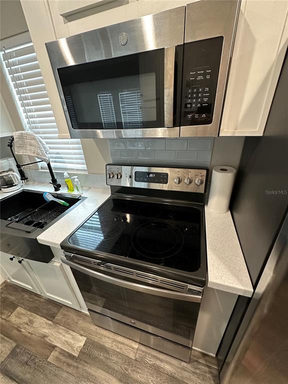 A kitchen features a stainless steel microwave, electric range, white cabinets, and a farmhouse sink — 16540 SUNSHINE AVENUE, CLERMONT, FL