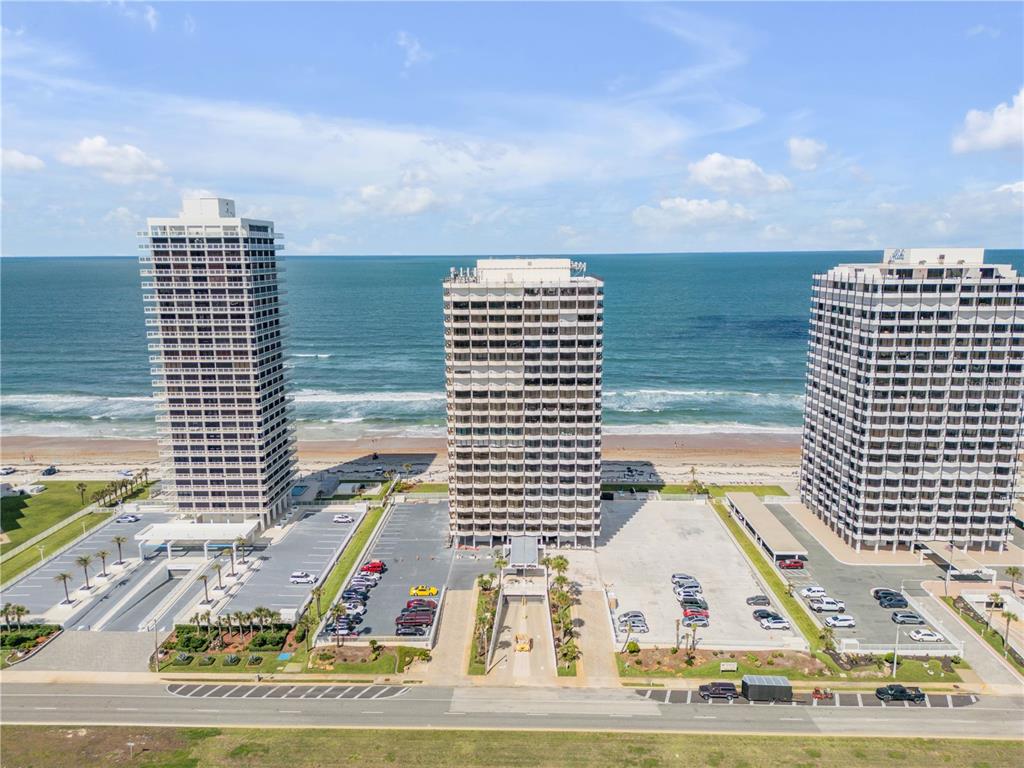 An aerial view shows three tall beachfront apartment buildings with parking lots along the coast — 2900 N ATLANTIC AVENUE UNIT 2106, DAYTONA BEACH, FL