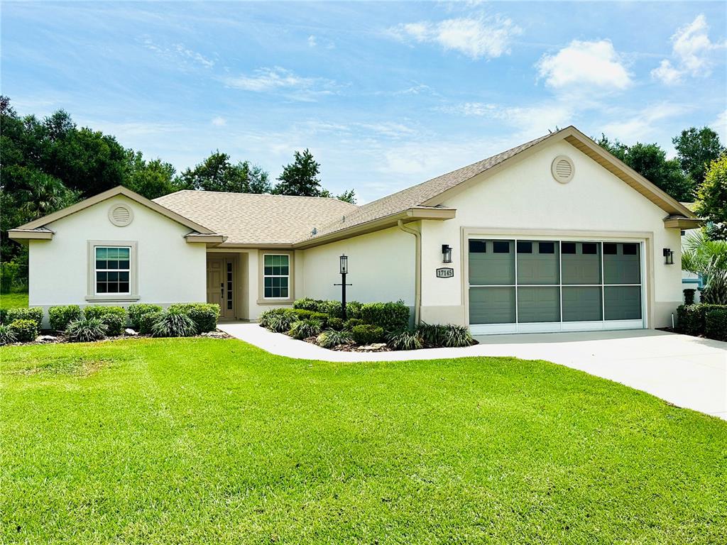 A single-story house with a beige stucco exterior, a two-car garage, and a green lawn — 17145 SE 113TH AVENUE, SUMMERFIELD, FL