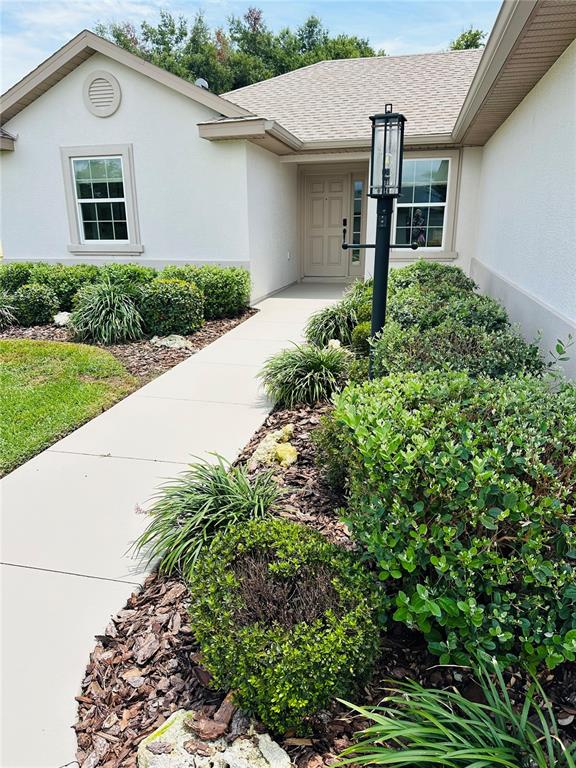 A concrete walkway leads to the front entrance of a house with light-colored siding — 17145 SE 113TH AVENUE, SUMMERFIELD, FL