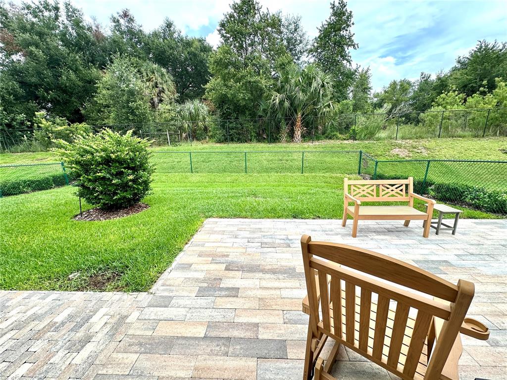 A backyard patio features stone pavers, a wooden bench, and a green lawn with fencing — 17145 SE 113TH AVENUE, SUMMERFIELD, FL