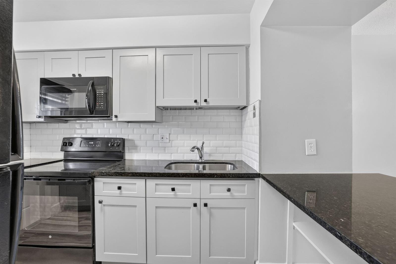 A kitchen features light gray cabinets, black appliances, dark countertops, and a white subway tile backsplash — 801 Pine Drive # 12, Pompano Beach FL 33060, POMPANO BEACH, FL