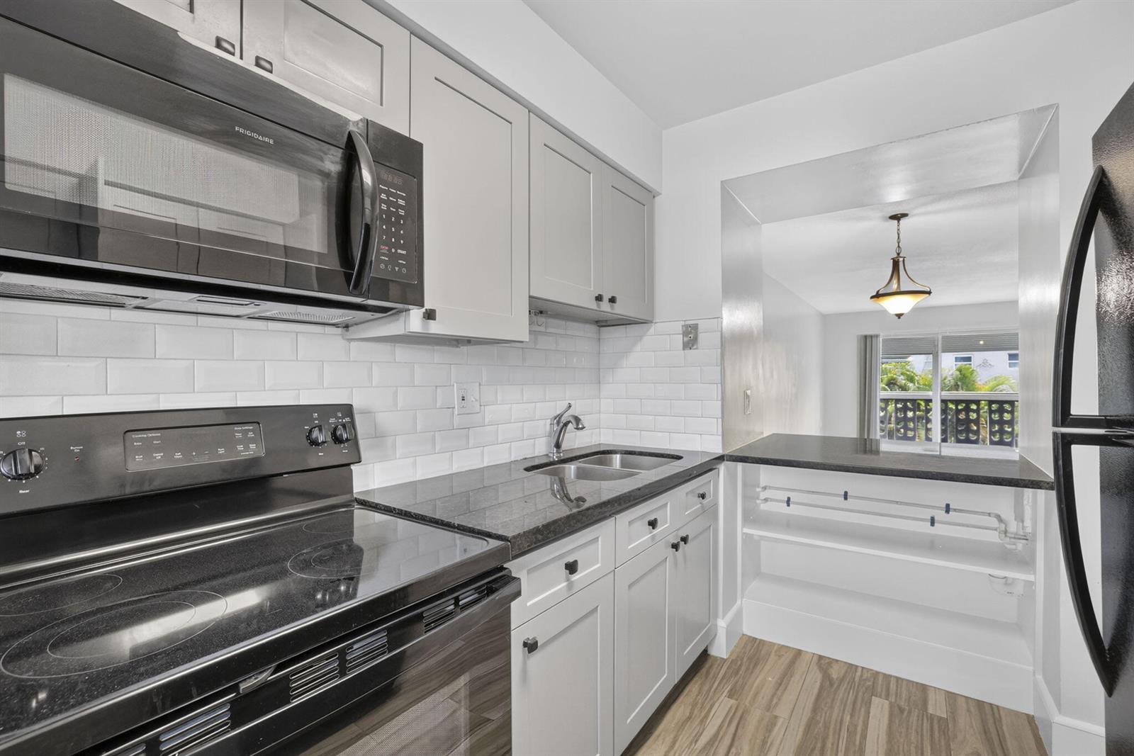 A kitchen features light gray cabinets, black appliances, dark countertops, and white subway tile backsplash — 801 Pine Drive # 12, Pompano Beach FL 33060, POMPANO BEACH, FL
