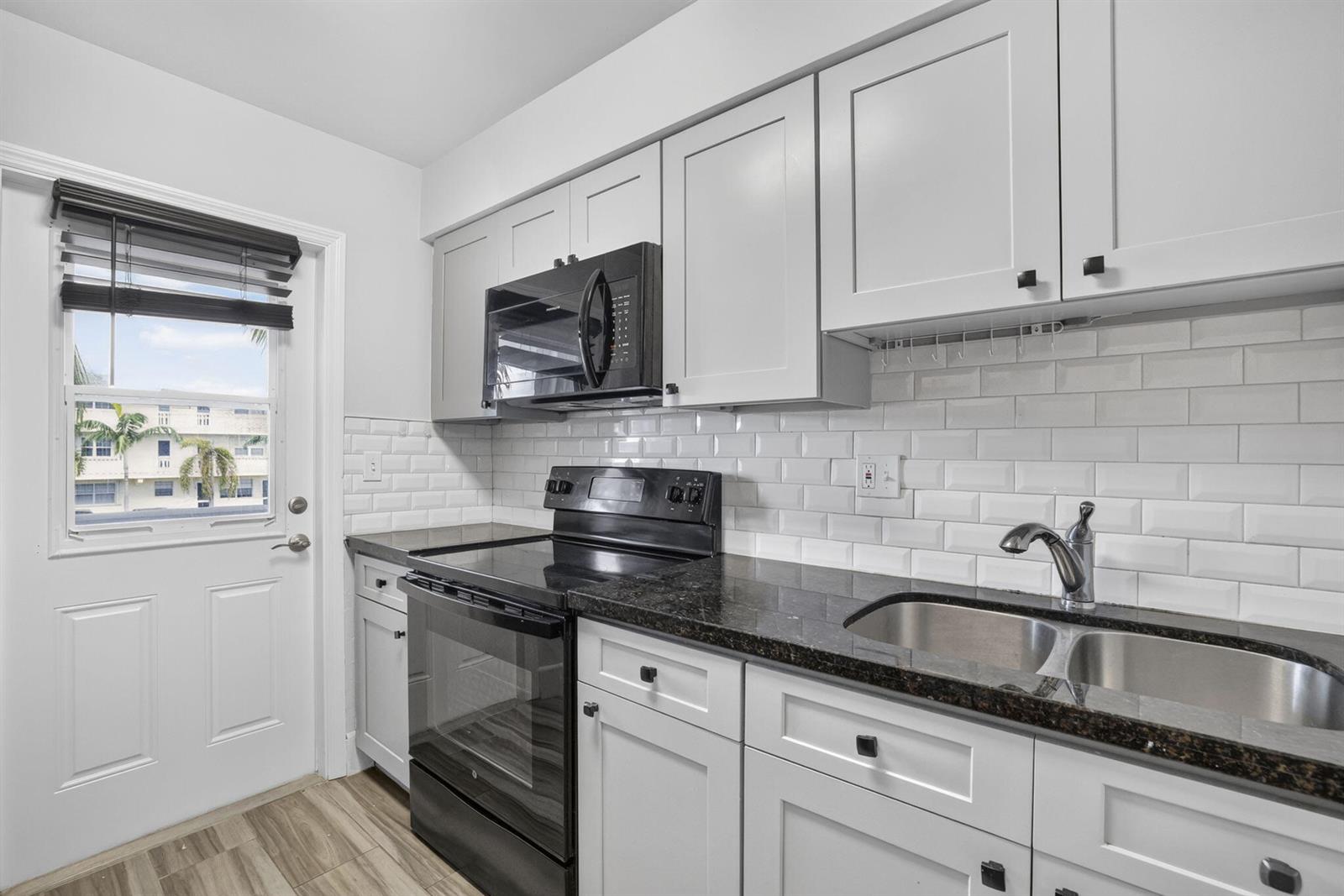 A kitchen features white shaker cabinets, black appliances, dark granite countertops, and white subway tile — 801 Pine Drive # 12, Pompano Beach FL 33060, POMPANO BEACH, FL