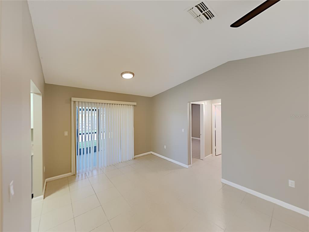 An empty room with light-colored tile flooring, beige walls, and a sliding glass door — 4128 SUNNY LAND DRIVE, LAKELAND, FL